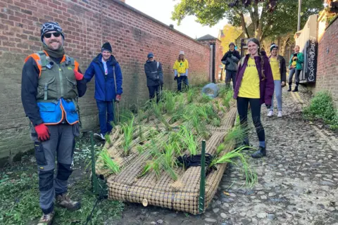 BBC / Naj Modak Volunteers standing by a pontoon-like structure with vegetation planted in it