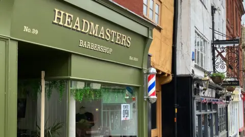 A close up of a barbershop shop in Gloucester city centre with a sage green frontage.