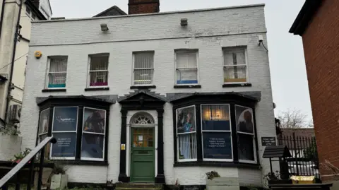 George King/BBC A white brick building with a green door. Age Well East signs can be seen within the windows