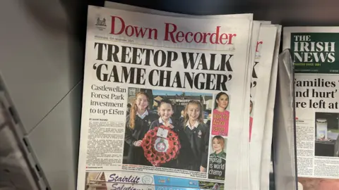 A pile of Down Recorder newspapers are on top of each other. The headline is Treetop Walk Gamechanger. There a photo of young people with a poppy wreath on the front page.