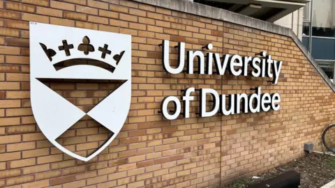 A white sign with a crest and the words University of Dundee on a brick wall