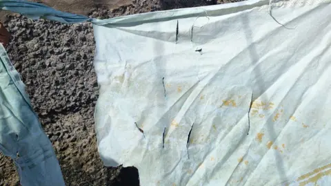 Nikita Goddard A sail which has at least eight straight cuts on it, as well as many yellow stains.