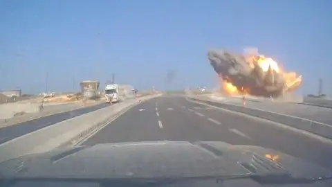 A road with a large explosion happening at the side of it