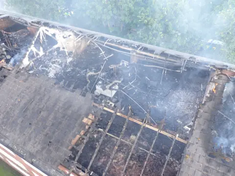 London Fire Brigade Aerial view of damaged roof of black of flats with smoke rising