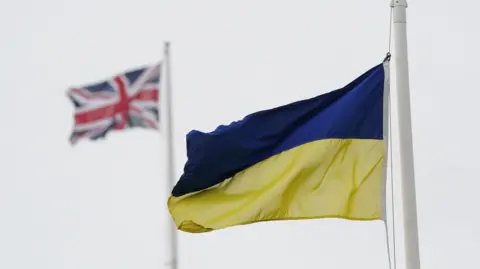 PA Media A Ukrainian flag flying from a flagpole. In the distance is a union jack flying from another flagpole.