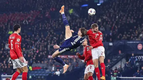 Getty Images Scotland footballer in a blue strip produces and overhead kick as three Denmark players in red tops and white shorts try to challenge him
