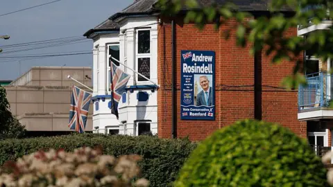 Getty Images The side of a large suburban villa - there is a large poster attached to the exterior wall that says Andrew Rosindell and Vote Conservative. 