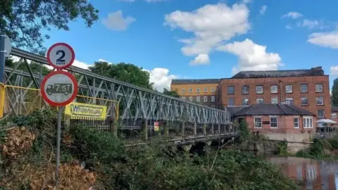 A bridge on top of another bridge in front of some historic mills.