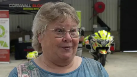 Magi Omlo-Coad looking to the right smiling at the camera. There is a blood bike stationary behind her. 