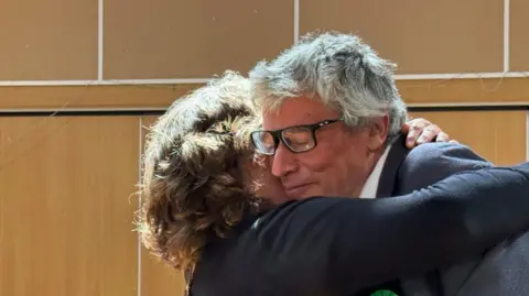 Lousie Parker/BBC A man is hugging a woman tightly and he has a relieved look on hsi face 