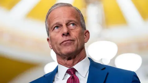 John Thune wearing a blue suit and red tie. 