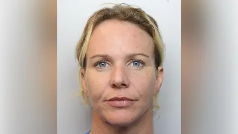 A mugshot of a woman with tied-back blonde hair and a blue shirt.