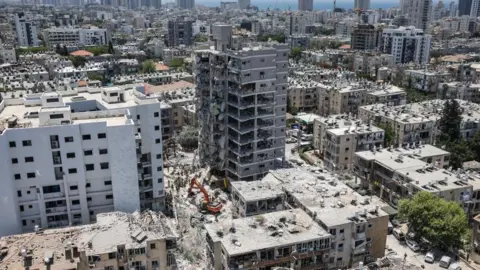 A landscape shot of a residential area with buildings damaged and rubble on the ground.