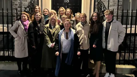 Hilltops Ukrainian Support Community A group of people stand together at night in front of the black door of 10, Downing Street. The doorway and house has an iron archway and railings in front of it.