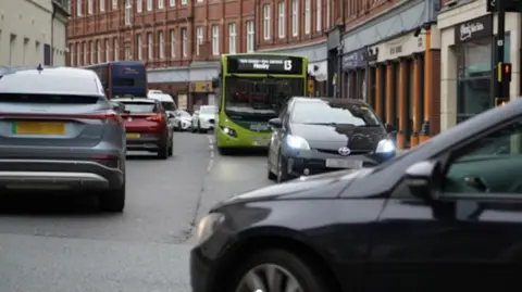 This is an image of buses caught in heavy traffic on York's Rougier Street. The street is part of the city centre's proposed bus priority area, which would be open only to buses and emergency vehicles. The traffic is stationary in both directions and a car is blocked as it waits to turn right into Rougier Street.
