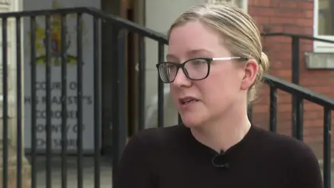 Cheri McDonald, wearing black glasses and a black top, speaks to a BBC reporter