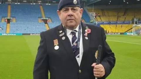 Blind Veterans UK Chris Fella on the pitch at Elland Road. Mr Fella is wearing his blue military beret and medals, a blue jacket and regimental tie