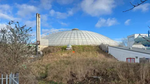 A derelict leisure centre bowl surrounded by long grass
