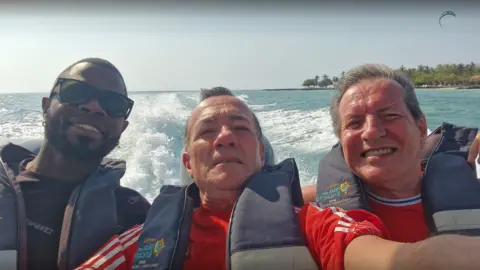 L-R Yostin Mosquera, Albert Alfonso and Paul Longworth. They are shown smiling in a selfie, all wearing life jackets as they sit at the back of a speedboat.