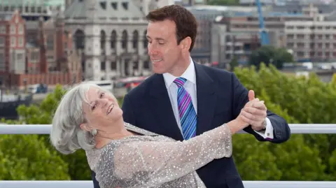 Ann Widdecombe dances with Anton du Beke in a ballroom pose with London skyline in background