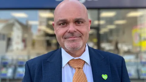 A man in a suit and tie smiling slightly into the camera