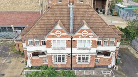 CAD Aerial A red brick building with two gable ends and white window frames, in Hackney, London. It is in a sate of disrepair. 