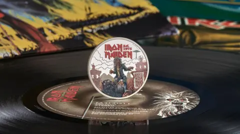 The commemorative balanced on its edge on top of an Iron Maiden vinyl record.