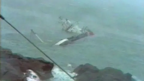 An aerial image of the Cita half submerged in the sea with rocks in the foreground
