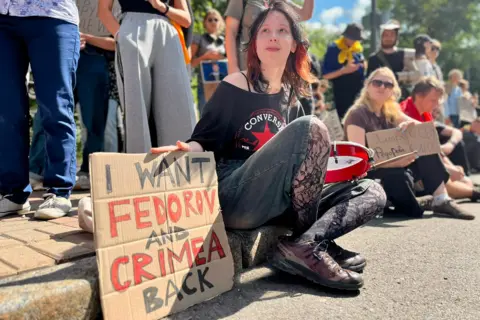 BBC/Isabella Jewell A woman sits beside a placard saying "I want Fedorov and Crimea back"