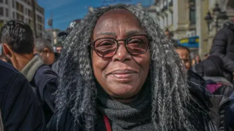 A person with grey, shoulder‑length hair in a crowded street during a march organised by the Tunisian General Labour Union (UGTT) in Tunis, surrounded by other participants and urban buildings in the background.