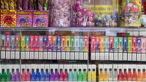 PA Media Disposable vapes on display on shop shelves below jars of sweets