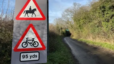 A country lane with two warning signs for drivers about horses and cyclists