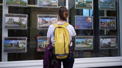 Woman looks at advertisements for houses in a window