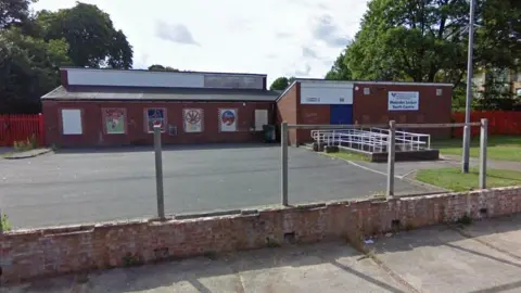 Google A single-storey brick building with a tarmac yard at the front. There is artwork on the walls and a Birmingham City Council sign reading "Malcolm Locker Youth Centre" 