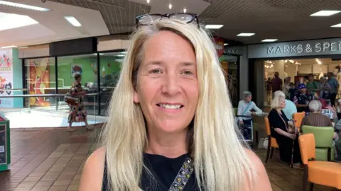 A woman with long, blond hair and wearing a pair of sunglasses on her head and a black sleeveless top 