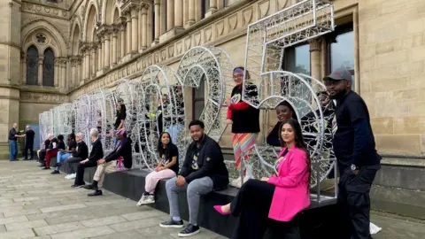 People sitting and standing among metal letters and numbers that spell out Bradford 2025