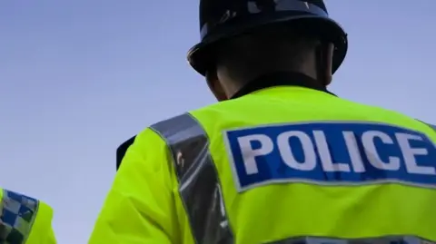 Getty Images A police officer is stood with his back towards the camera. He is wearing a yellow hi-vis jacket with "police" written on the back.