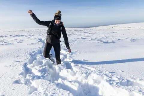 Jamie Rutherford/Montane Spine Race A woman runs through deep snow. She is dressed all in black with a headband