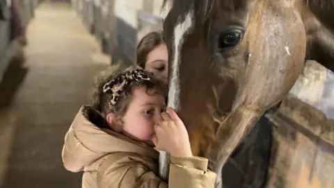 Family photo Betsy kisses Kitty's Light in the stables with her sister Tilly alongside her