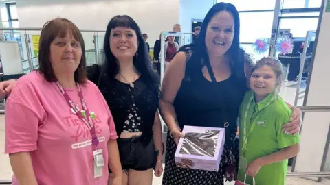 Asda Three women and a young girl stand together. The girl, on the right, is wearing a green Asda uniform.