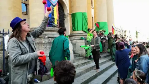 A crowd of people watch street performers juggling on the steps of a building in central Oxford as part of May morning celebrations 