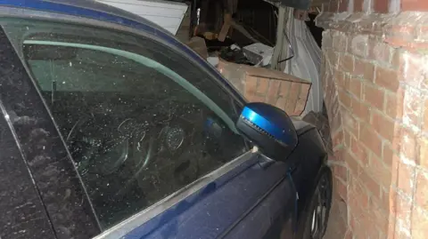 Contributed The front driver's side of a blue car has been pushed into brickwork on a wall of a garage. Bits of broken brickwork are on the car's bonnet.