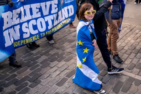 PA Media A young girl - draped in a saltire flag - takes part in a march and rally for independence organised by Believe in Scotland, which aims to celebrate Scotland's potential, its culture and its people in Edinburgh.