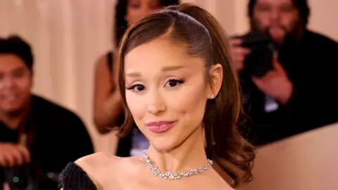 Ariana Grande poses for the cameras at the Golden Globes earlier this year. She is wearing a black dress and diamond necklace and has her hair in a ponytail.