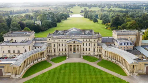 Stowe House Aerial view of a large stately home with a grand central building in a horseshoe shape, surrounded by manicured lawns and expansive parkland stretching into the distance.