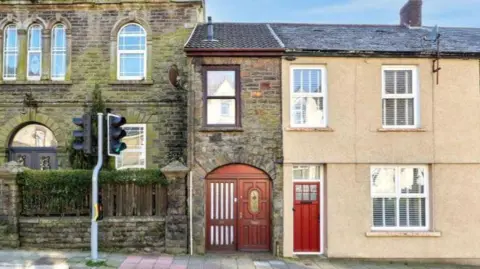 A general view of property on Llewellyn Street. It is a brick house with a wooden door and window frame. The house sits on the main street in front of a set of traffic lights.