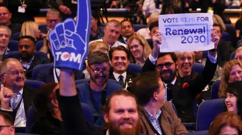 Getty Images A bearded man in the audience at the Tory conference smiles as he holds up a foam finger