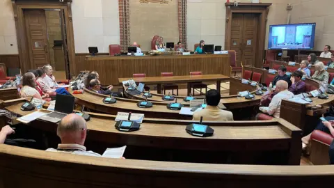 The inside of Cambridge City Council's Guildhall, with councillors sitting at desks with microphones in front of them.