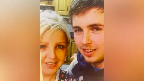 Edwina Thompson-Clarke A selfie of Edwina Thompson-Clarke with her son Daryl Thompson. They are stood in a kitchen and both are smiling at the camera. There are large blurred boxes on either side of the vertical photo.