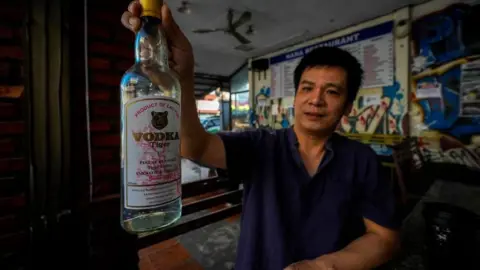 AP Duong Duc Toan, the manager of Nana Backpack hostel in Vang Vieng, holds a bottle of Tiger vodka in the hostel's bar